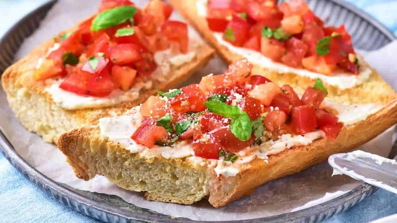 Slices of toasted bread topped with cream cheese, diced tomatoes, chopped herbs, and a sprinkle of cheese on a plate make for one of the best fresh tomato dishes—perfect for enjoying classic summer tomato recipes.