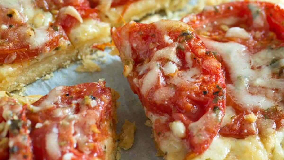 Close-up of a sliced tomato and cheese pizza with melted cheese and visible herbs on a thin crust—an inviting addition to your collection of garden tomato recipes.