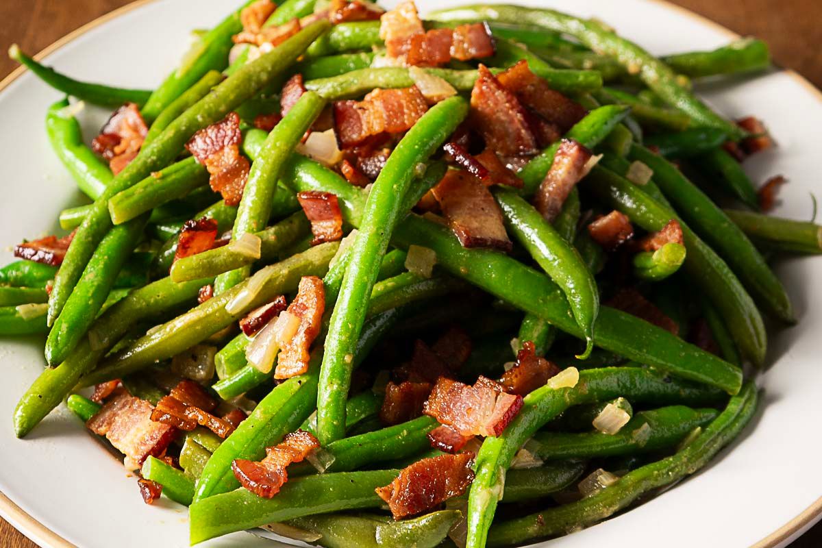 Plate of cooked green beans mixed with chopped bacon and small pieces of onion, making it one of those reader favorites that always stands out among popular side dishes.
