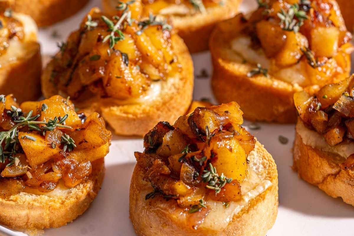 Toasted bread slices topped with cooked, diced apples and garnished with fresh herbs, this delightful creation is a perfect addition to your collection of apple recipes, beautifully arranged on a white plate.
