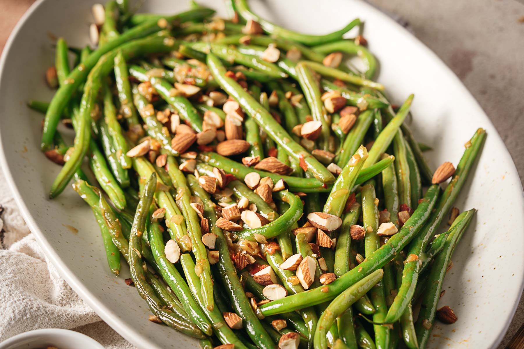 Green beans are served on a white oval plate, topped with chopped almonds—making this classic Side Dish one of our reader favorites.