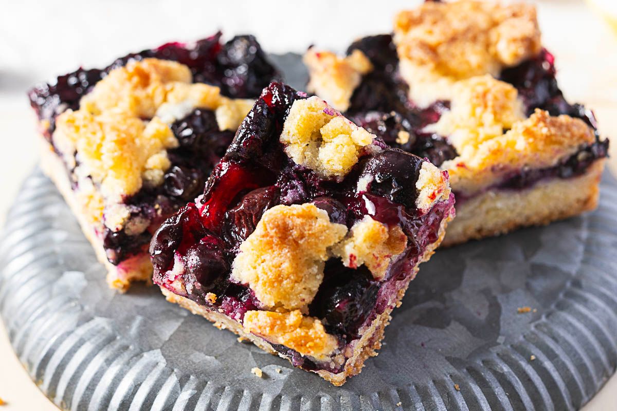 Two square blueberry crumb bars with golden topping rest on a gray plate—an easy dessert perfect for summer cookouts or Labor Day gatherings.