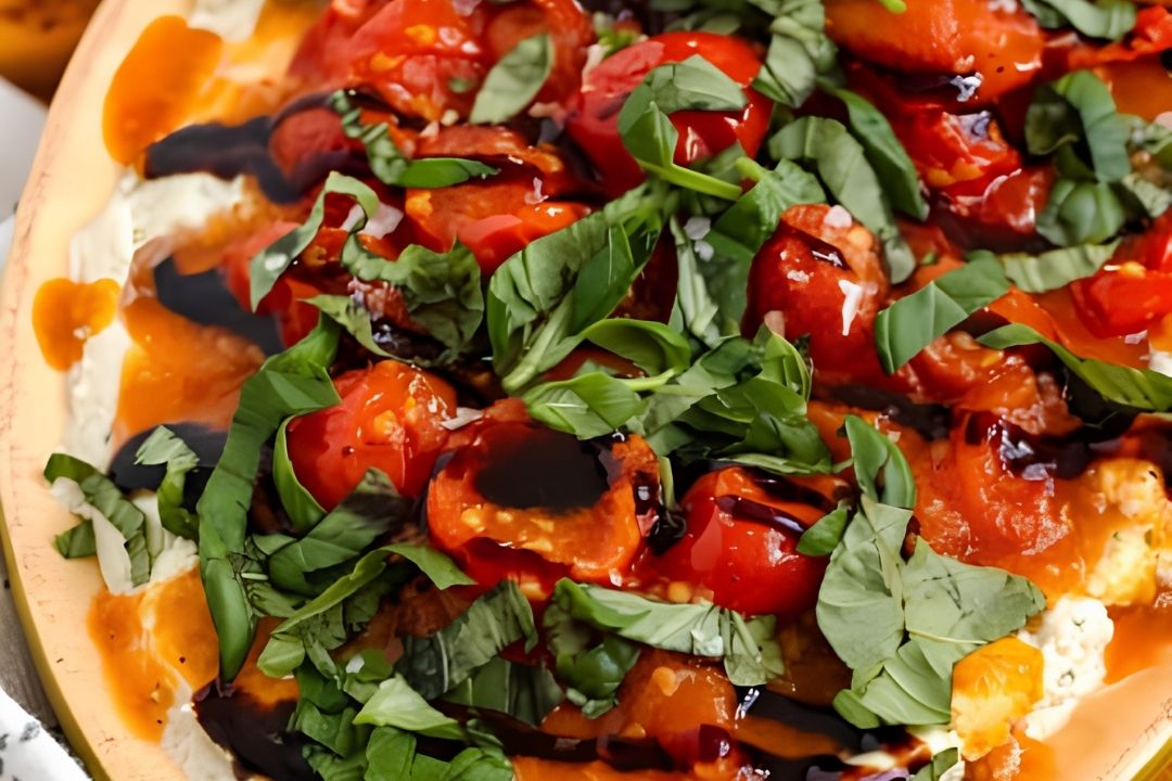 Close-up of a caprese-style dish topped with sliced cherry tomatoes, fresh basil leaves, ricotta cheese, and a drizzle of balsamic glaze—perfect for snacking or serving as one of your go-to game day snacks.