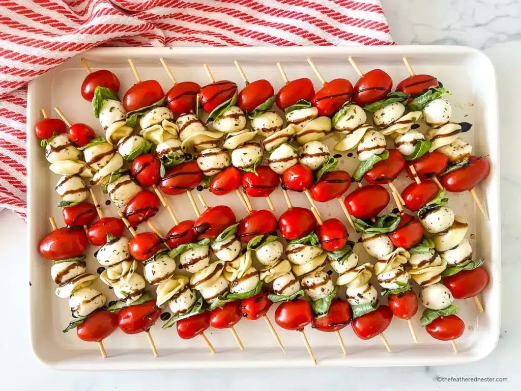 A tray of caprese skewers with cherry tomatoes, mozzarella balls, basil leaves, and balsamic glaze, arranged in neat rows—these travel friendly salads are perfect for parties or potlucks.