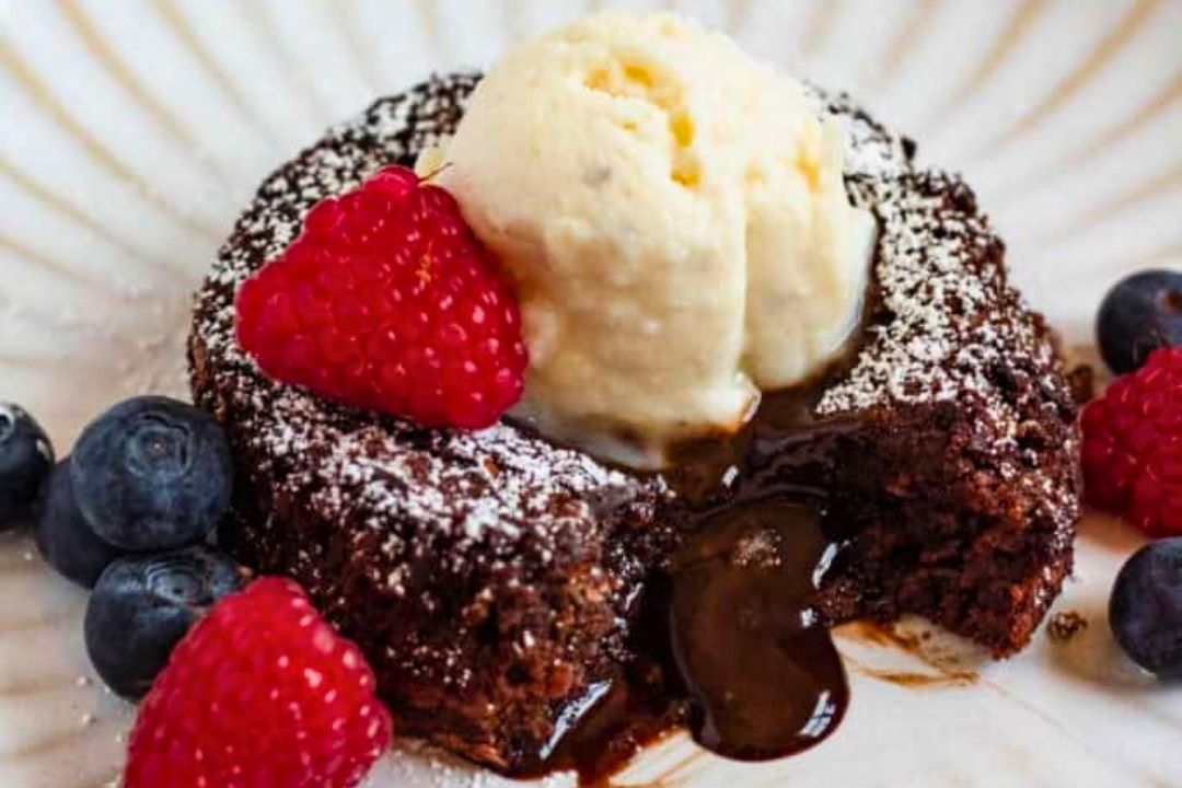 Chocolate lava cake with a scoop of vanilla ice cream, topped with powdered sugar, raspberries, and blueberries on a white plate—an irresistible treat perfect for chocolate lovers and a standout among dessert recipes.
