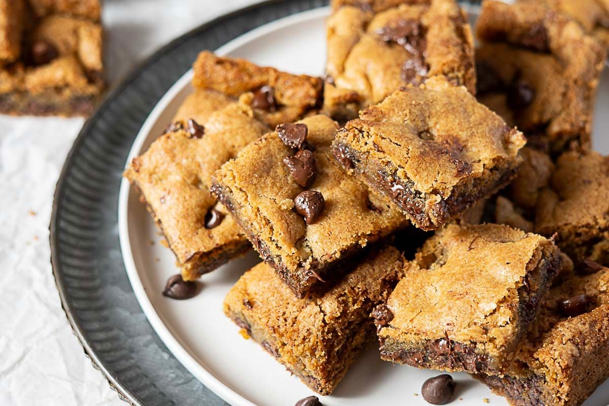 A plate of chocolate chip cookie bars stacked on top of each other, with visible chocolate chips scattered throughout the bars—these irresistible treats are perfect for any chocolate chip cookies lover.