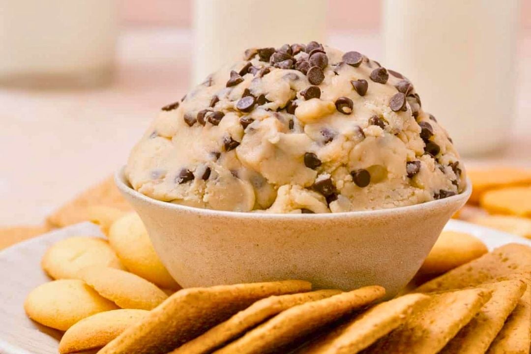 A bowl of cookie dough with chocolate chips, inspired by classic chocolate chip cookie recipes, is surrounded by vanilla wafer cookies and graham crackers on a plate—a delightful display of irresistible chocolate treats.