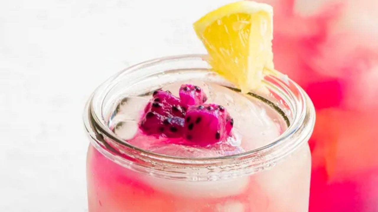 A glass jar filled with pink drink, ice cubes, dragon fruit pieces, and a lemon wedge on the rim—perfect to cool off with refreshing beverages this Labor Day.