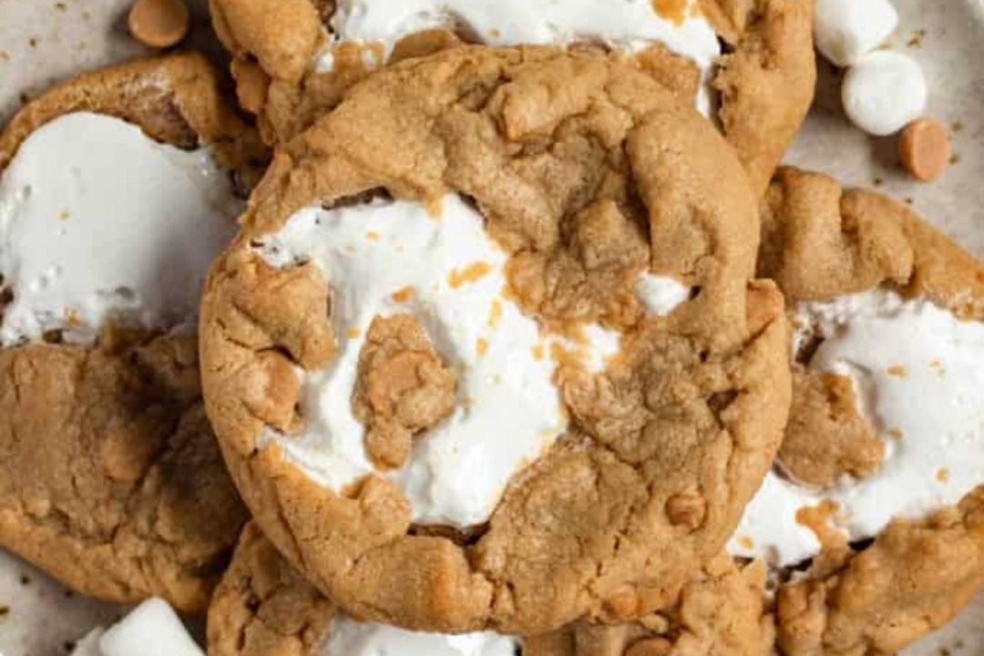 Close-up of several cookies with a golden-brown exterior, visible white marshmallow filling, and scattered butterscotch chips—a delicious addition to any lineup of peanut butter desserts.