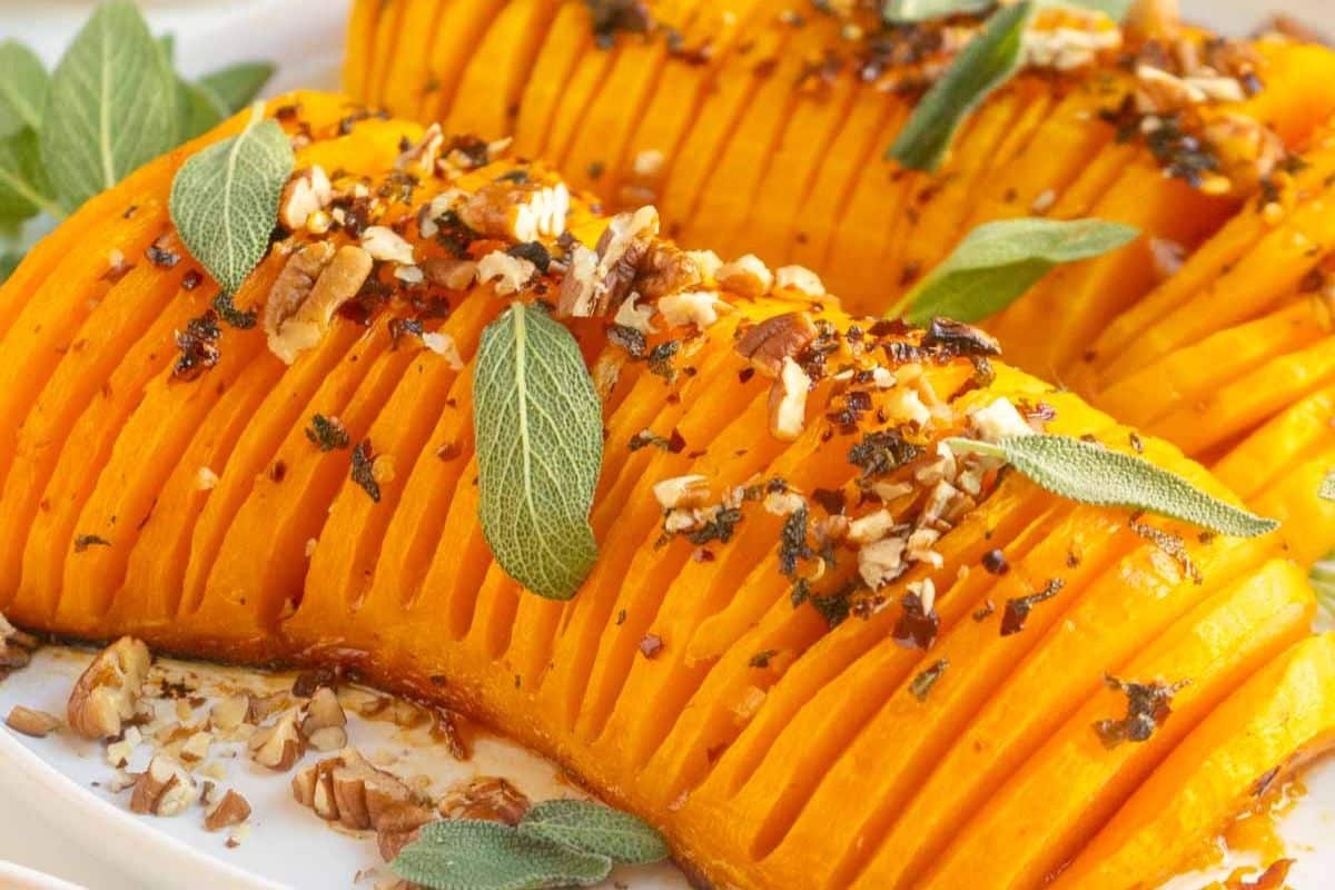 Sliced roasted butternut squash garnished with chopped nuts, fresh sage leaves, and seasoning on a white plate—perfect for adding to your collection of cozy fall recipes or autumn meals.