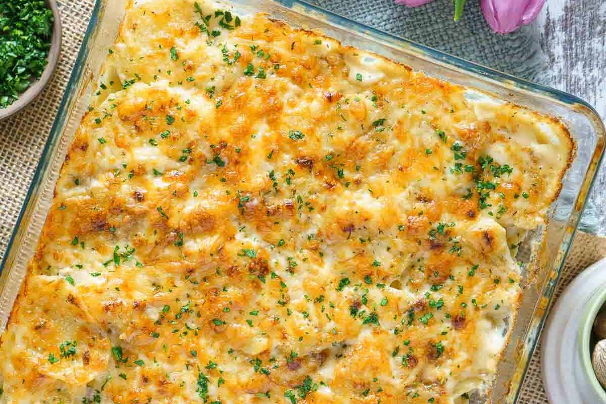 Baked casserole in a glass dish topped with melted cheese and chopped herbs, shown from above on a rustic surface—a perfect gluten-free dish to add to your collection of Labor Day recipes.
