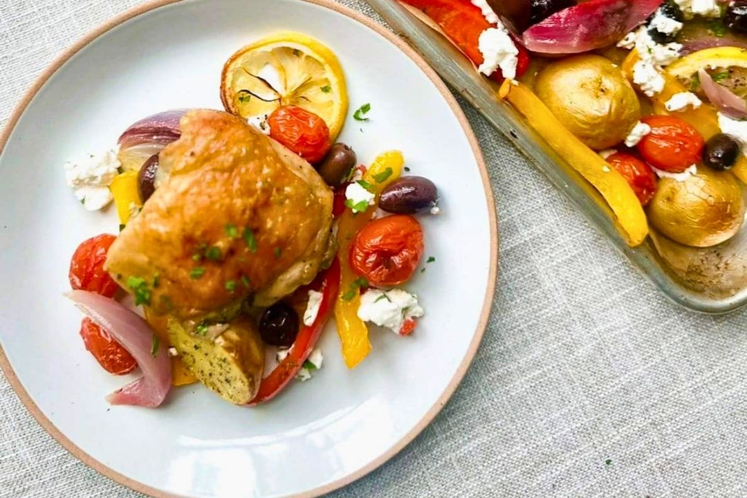 A perfect example of easy dinners, this plate features roasted chicken, cherry tomatoes, olives, red onions, yellow peppers, potatoes, feta cheese, and a slice of lemon—served alongside a dish brimming with the same vibrant ingredients. Ideal for busy weeknight meals or those who love flavorful sheet pan meals.