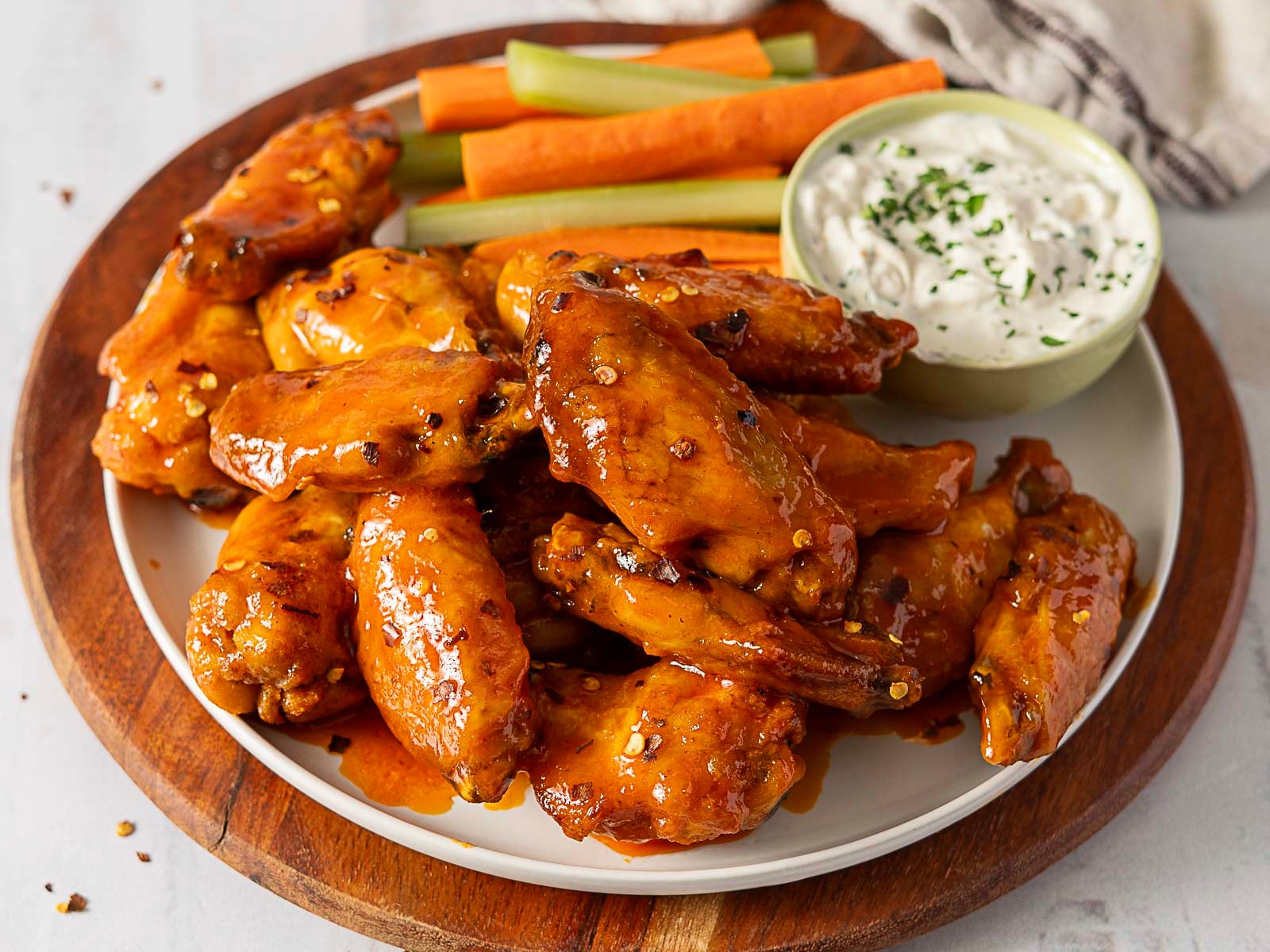 A plate of saucy chicken wings with carrot and celery sticks, served with a side of ranch dip on a wooden board—perfect for those seeking crowd-pleasing Game Day Appetizers.