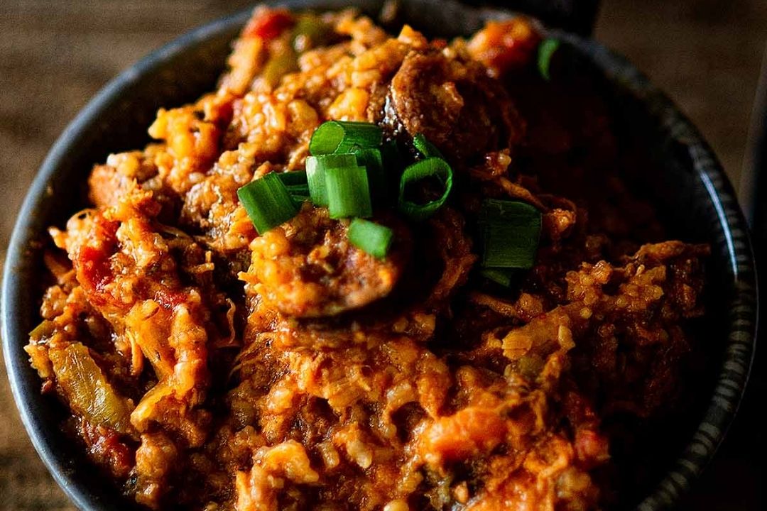 A close-up of a bowl filled with jambalaya, featuring rice, sausage slices, vegetables, and topped with chopped green onions—perfect for those seeking comforting fall recipes or easy crockpot recipes.