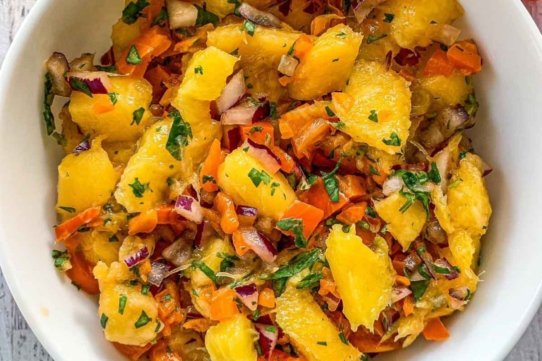 Bowl of salad with orange segments, chopped red onion, carrots, and fresh herbs mixed together.