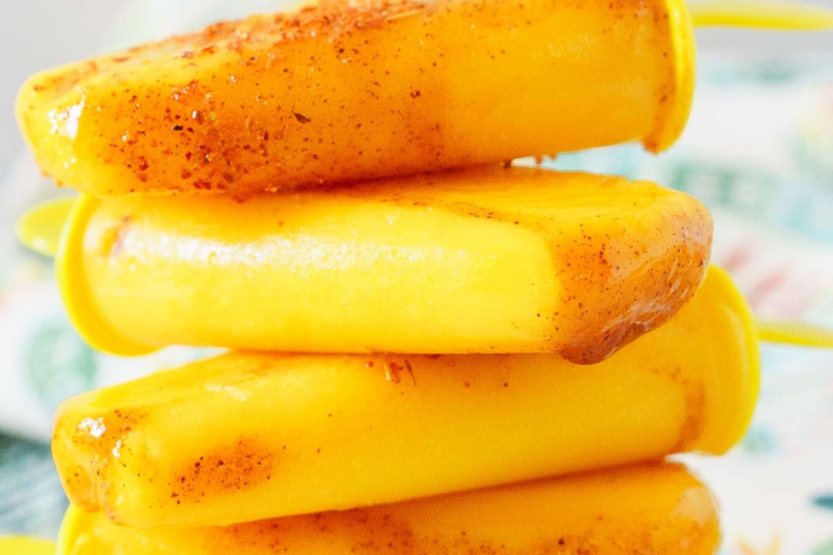 Three yellow popsicles stacked on top of each other, dusted with a reddish-brown spice, shown close up—a refreshing treat that’s perfect for Labor Day recipes and completely gluten-free.