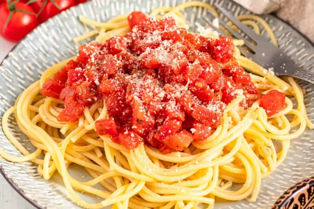 A plate of spaghetti topped with tomato sauce and grated cheese, served with a fork on a patterned plate.