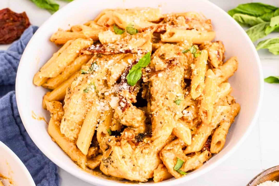 Bowl of creamy penne pasta with chicken strips, garnished with grated cheese and fresh herbs—perfect for cozy dinners and those seeking easy pasta recipes.