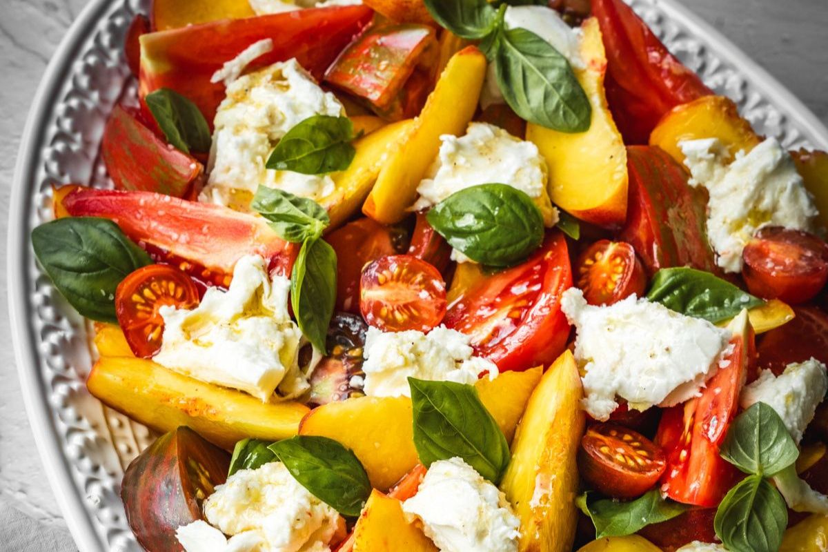 A platter with sliced tomatoes, peaches, fresh mozzarella, cherry tomatoes, and basil leaves arranged together—perfect for showcasing vibrant garden tomato recipes.