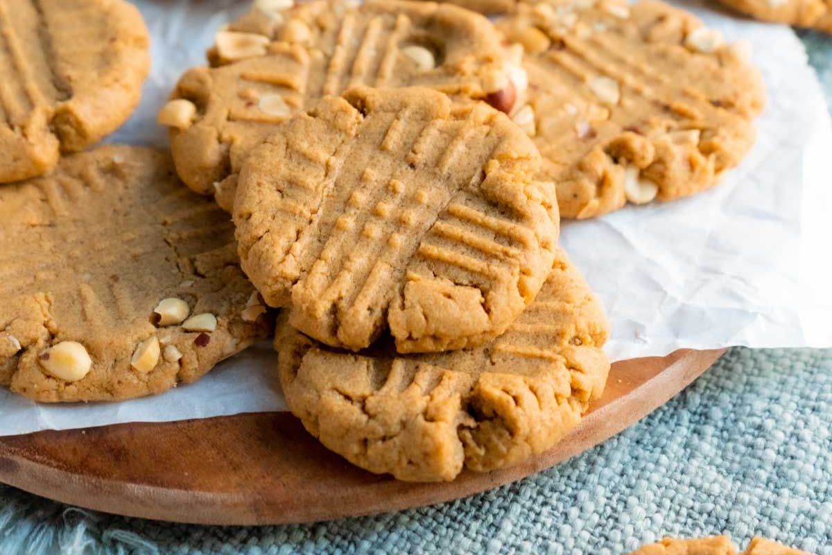 A close-up of several peanut butter cookies with a criss-cross fork pattern on top, arranged on parchment paper on a wooden tray—perfect treats for anyone searching for classic peanut butter recipes or delicious peanut butter desserts.
