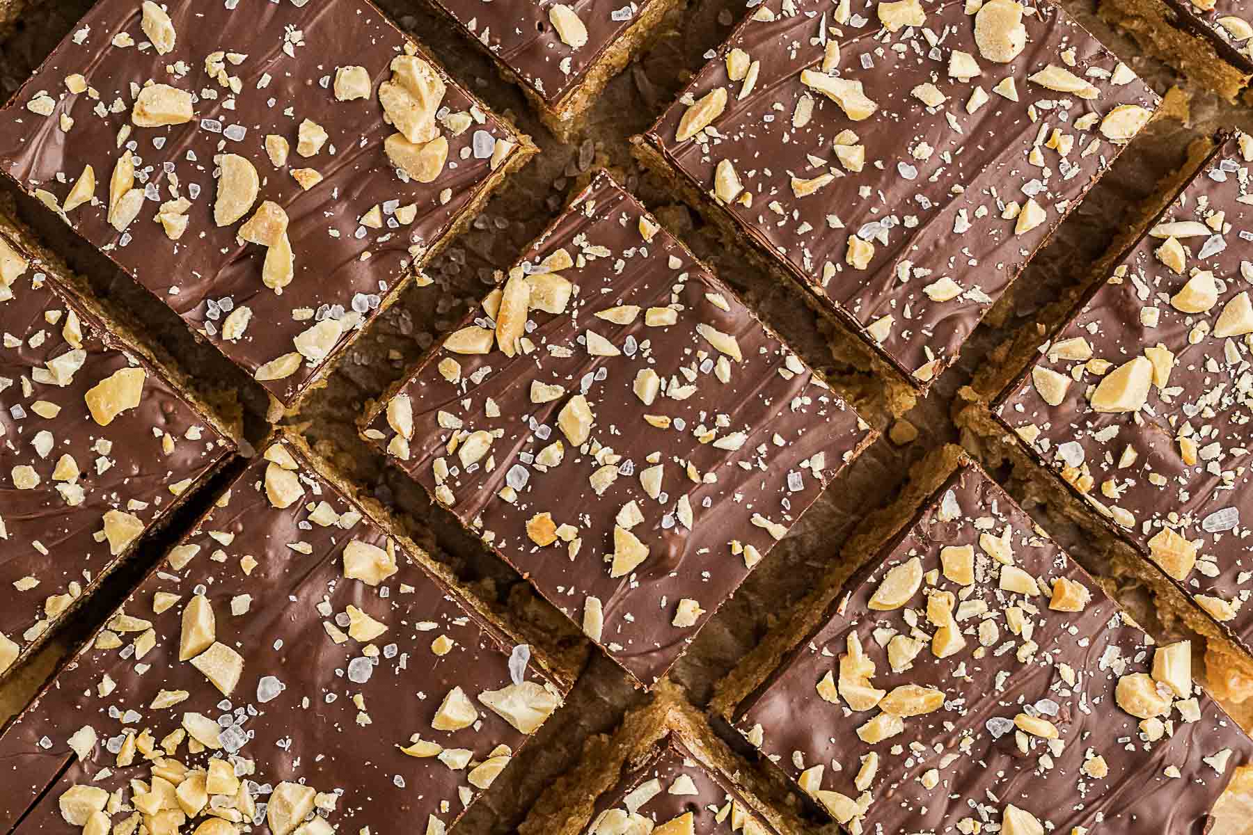 Nine square dessert bars topped with chocolate, chopped nuts, and sea salt, arranged in a grid pattern—a delicious twist on classic peanut butter desserts that will satisfy any sweet tooth.