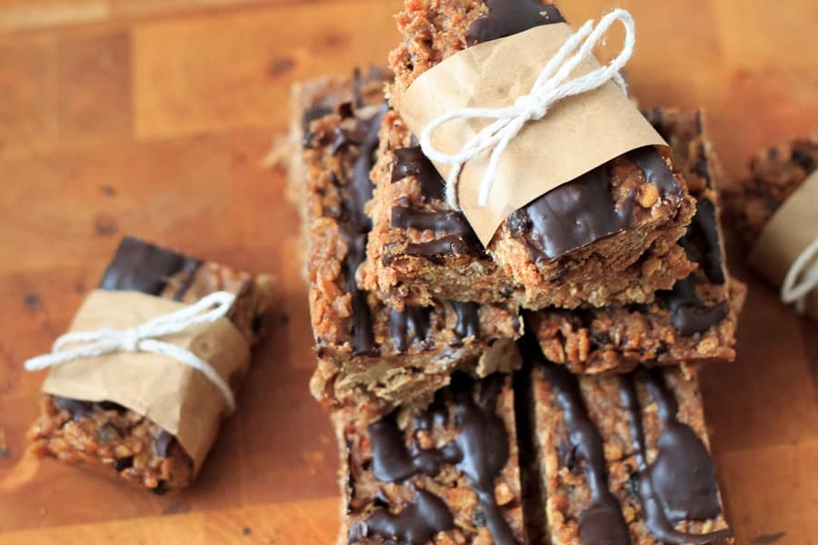 A stack of chocolate-drizzled granola bars, perfect for chocolate lovers, is tied with brown paper and string and sits on a wooden surface.