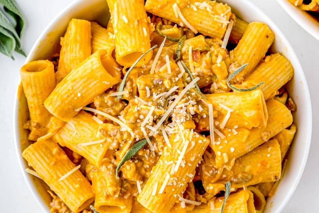 Bowl of rigatoni pasta topped with a creamy orange sauce, ground meat, shredded cheese, and sage leaves—perfect for cozy dinners and anyone who loves comforting pasta recipes.