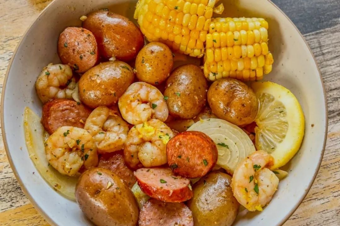 A bowl with shrimp, sausage slices, baby potatoes, corn on the cob, onions, and a lemon wedge—perfect for easy recipes or quick weeknight dinners.