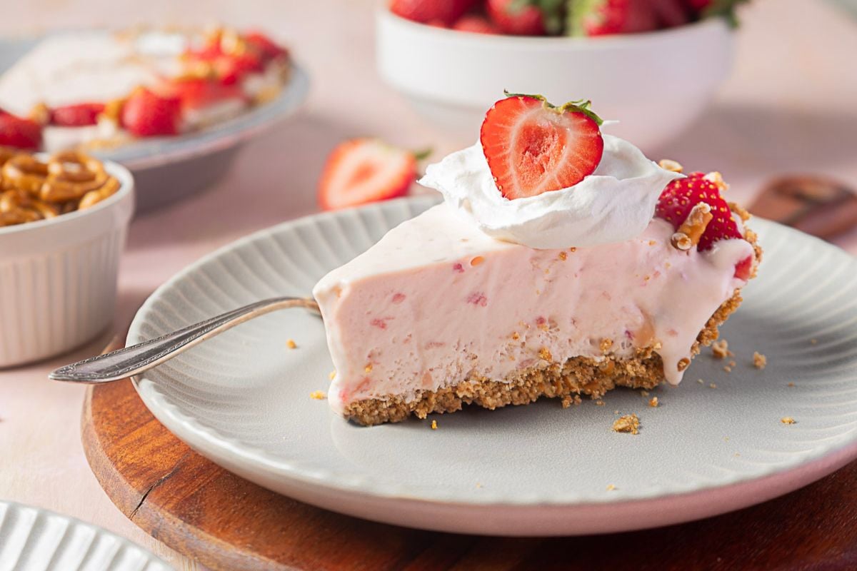 A slice of strawberry cream pie with whipped topping and a fresh strawberry on a plate, with a fork beside it—perfect for gluten free desserts and those seeking delicious summer desserts.