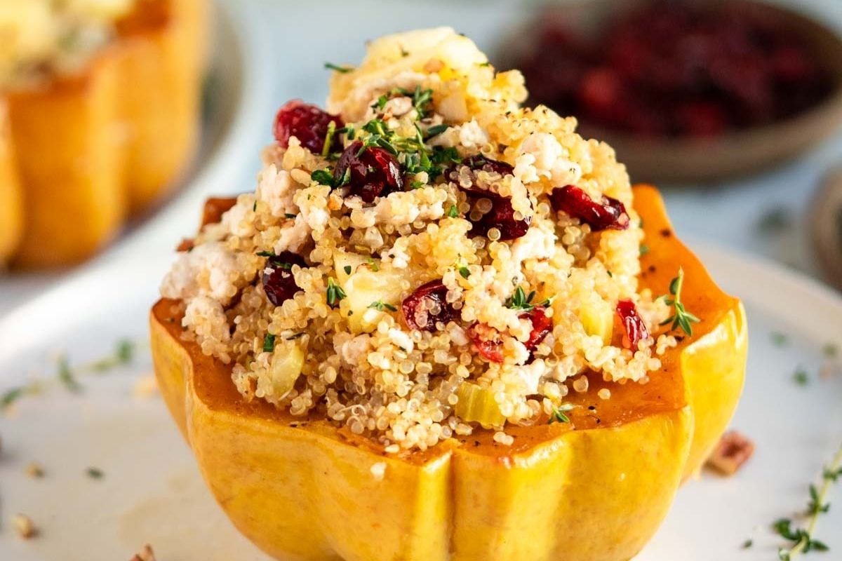 A baked squash half filled with a quinoa, cranberry, and feta cheese mixture, garnished with herbs and served on a white plate—perfect for those seeking delicious fall recipes or flavorful autumn meals.