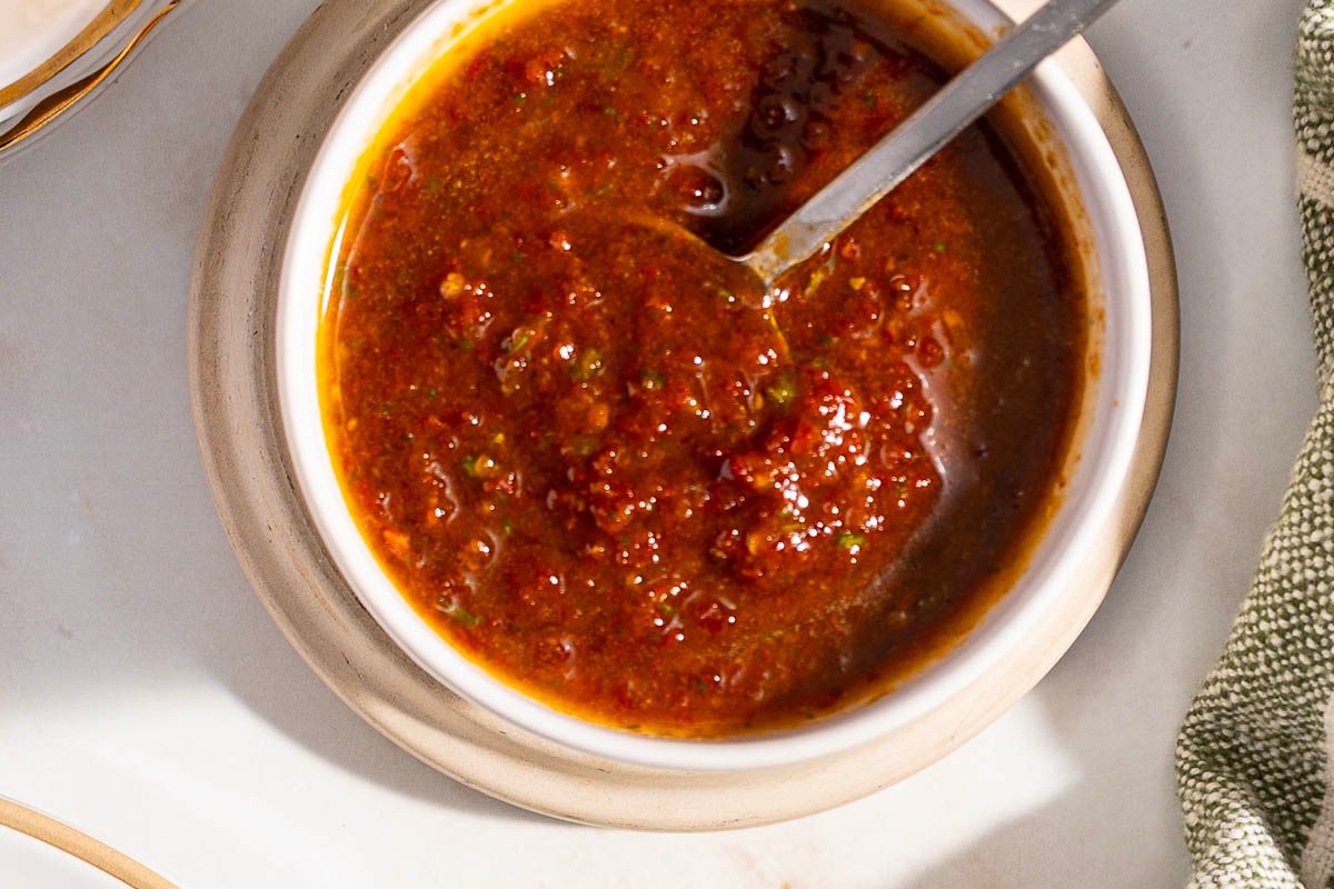 A bowl of red salsa with a spoon inside, placed on a saucer, perfect for those who appreciate homemade dressings and fresh flavor.