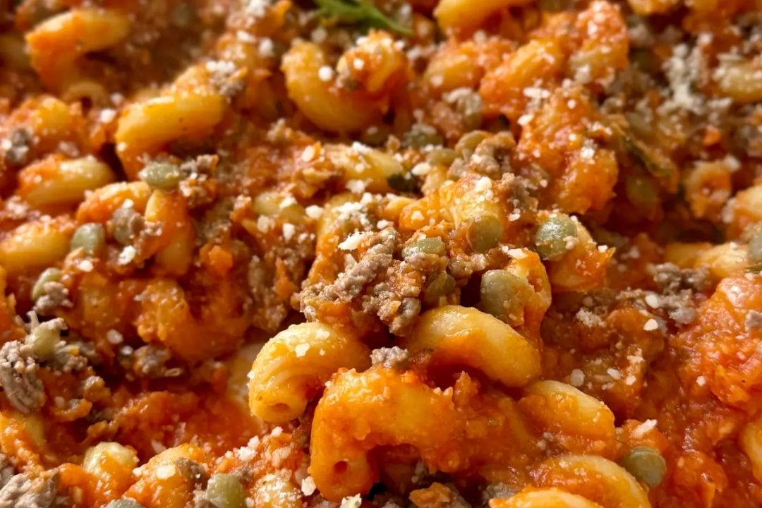 Close-up of macaroni pasta with ground meat, tomato sauce, green peas, and grated cheese sprinkled on top.