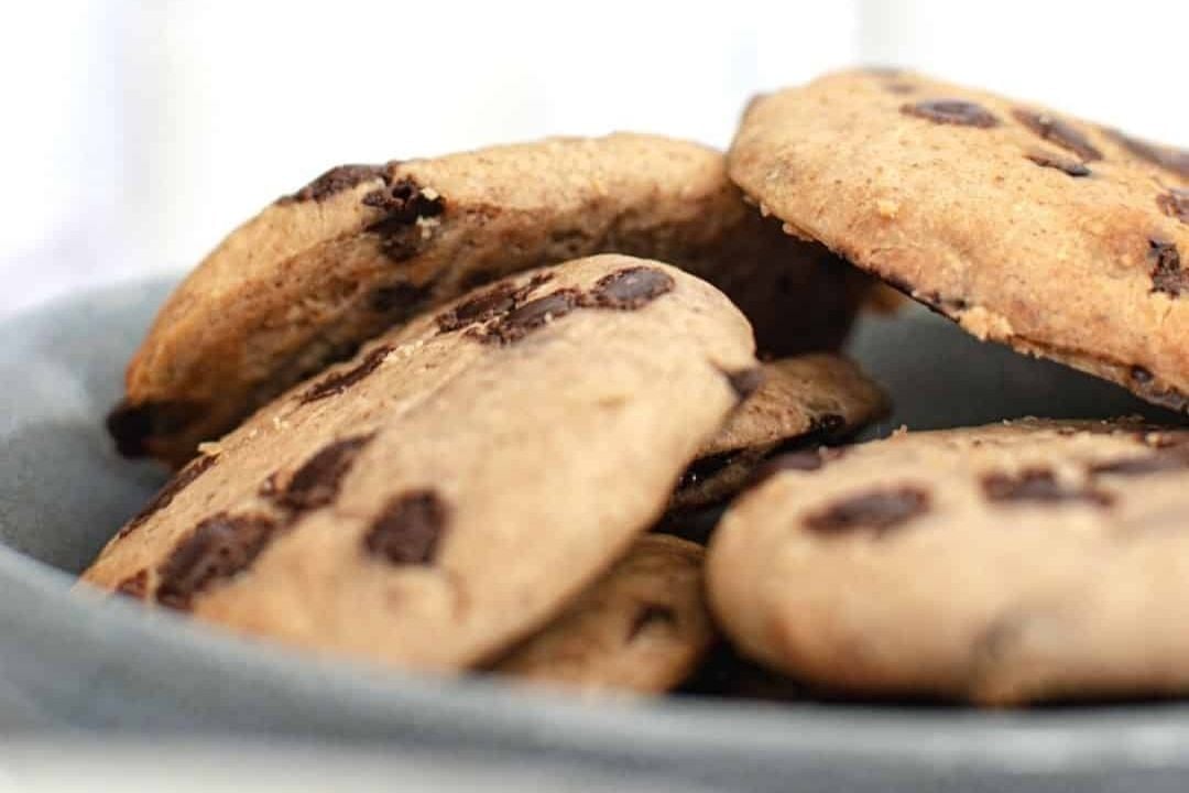 A close-up of several chocolate chip cookies, the classic chocolate treat, stacked on a gray plate.