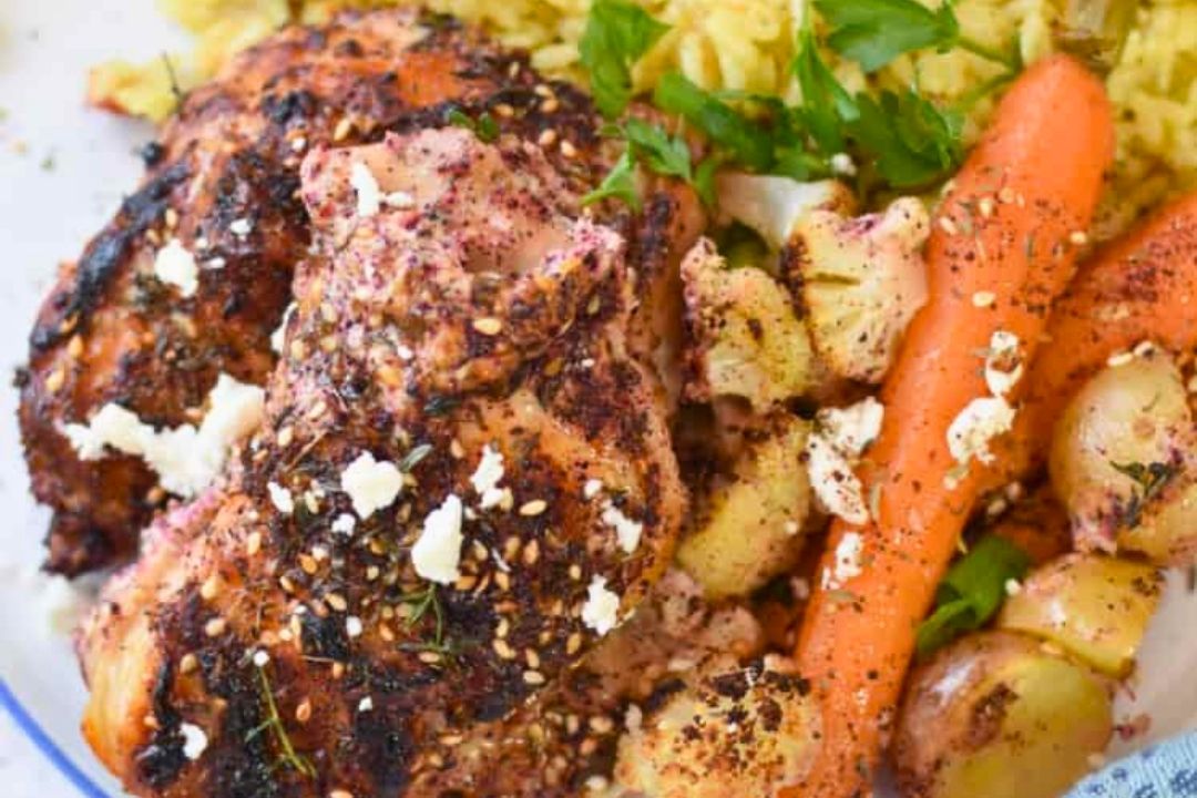 Seasoned roasted chicken—one of our standout new chicken dishes—is topped with sprinkled feta and served alongside yellow rice, carrots, and baby potatoes, then garnished with fresh herbs on a white plate.