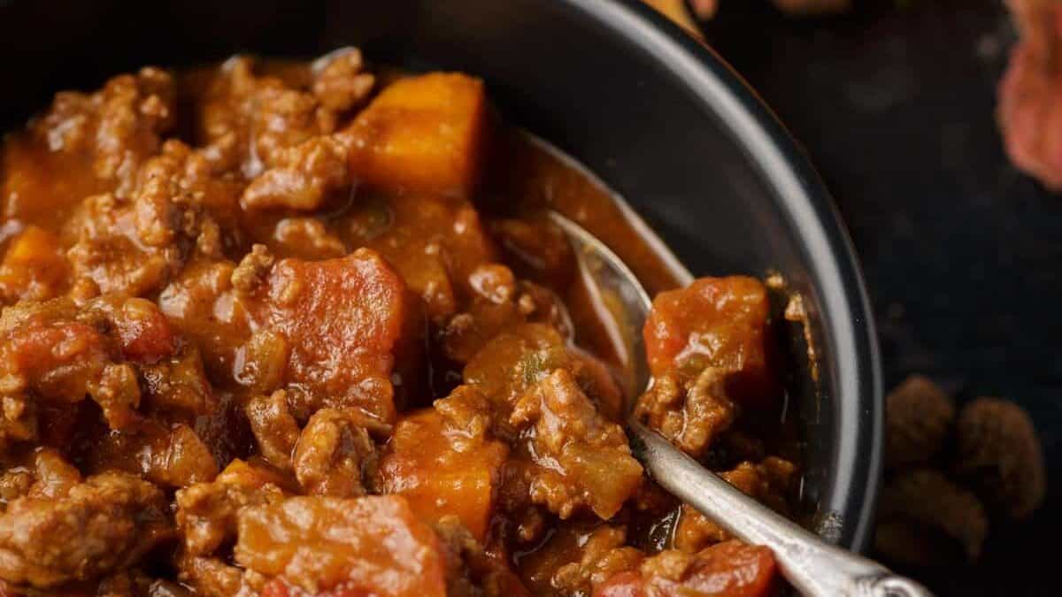 Close-up of a bowl of chili with ground meat, tomatoes, and vegetables—one of many hearty sweet potato recipes—with a spoon inside the bowl.