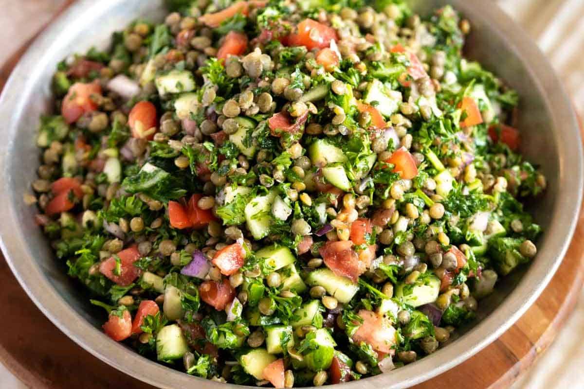 A bowl filled with lentil salad mixed with chopped tomatoes, cucumbers, onions, parsley, and herbs—a fresh and delicious option inspired by popular recipes.