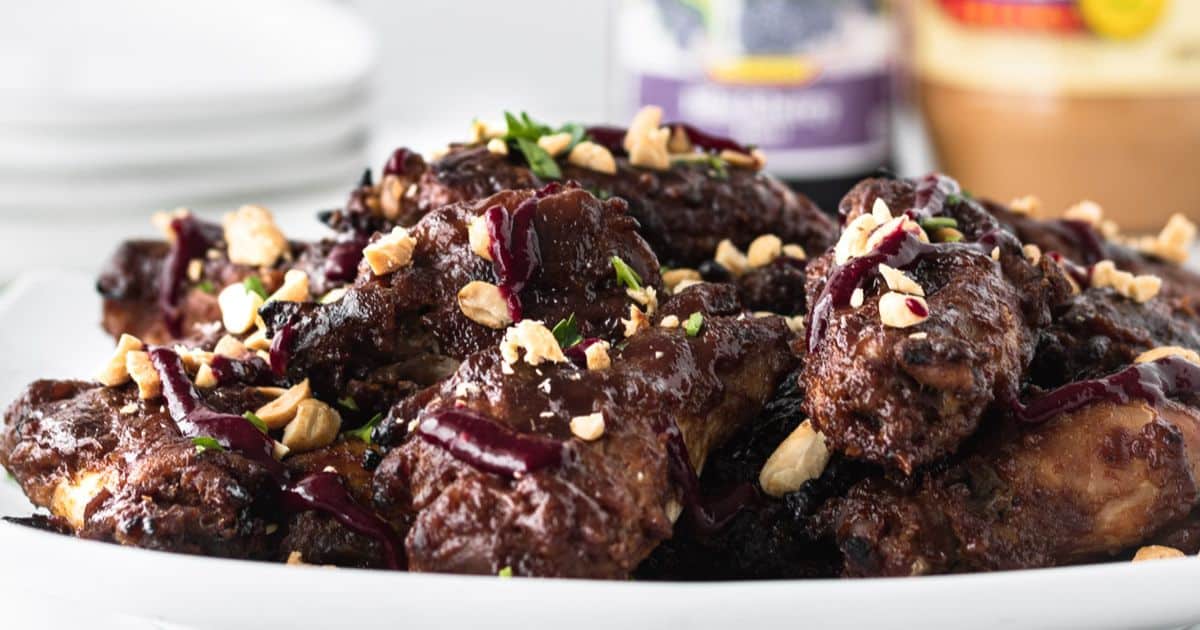 A plate of glazed chicken wings garnished with chopped nuts and herbs, perfect for halftime snacks, served on a white dish.