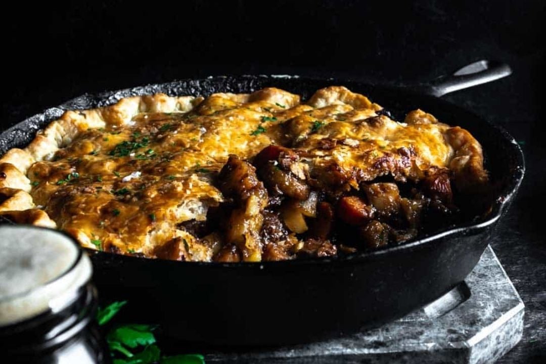 A golden-brown pot pie with meat and vegetables is baked in a cast iron skillet, perfect for Sunday night recipes or those who love cozy braises.