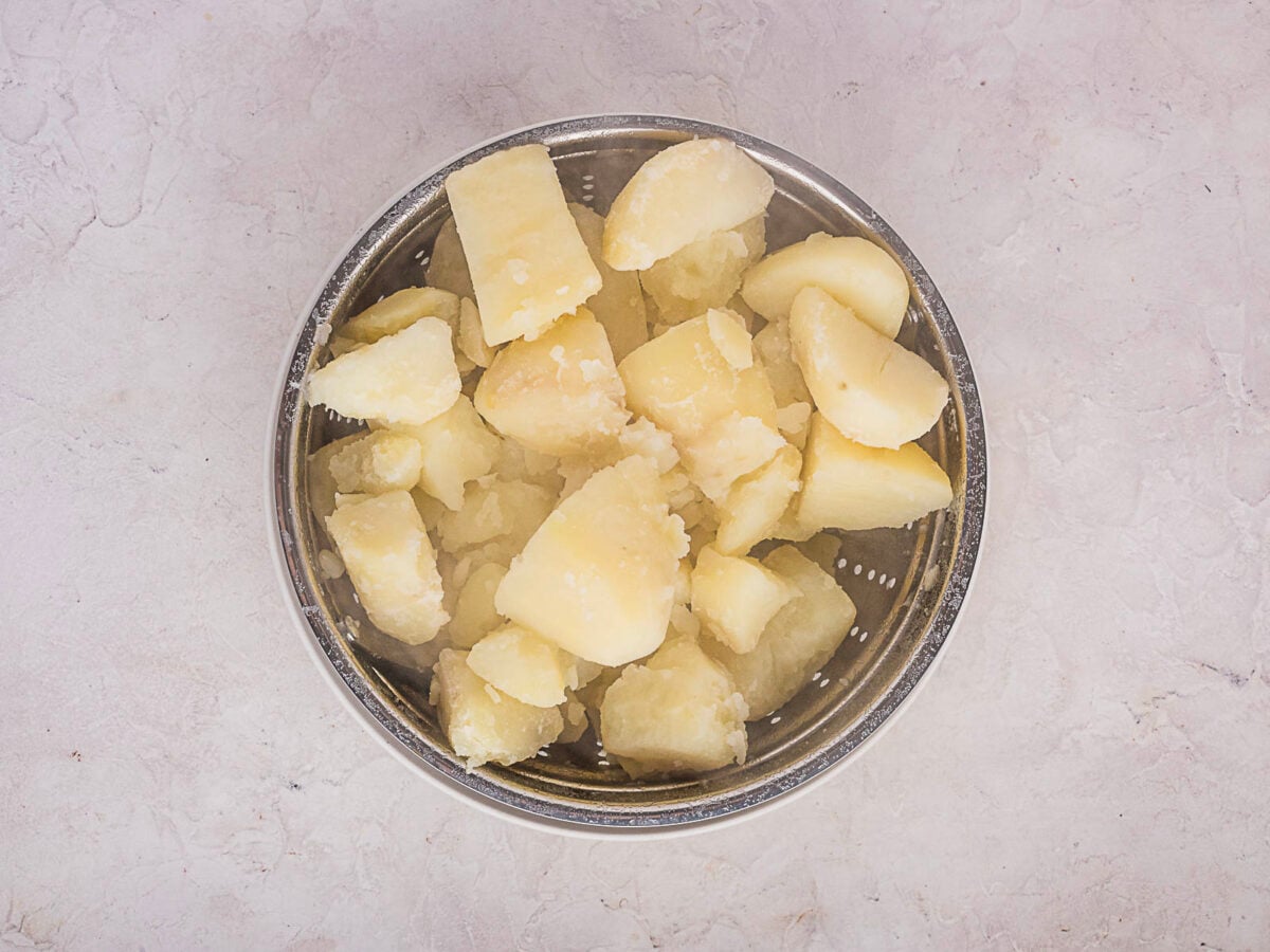 Boiled and chopped potatoes in a metal colander on a light-colored surface.