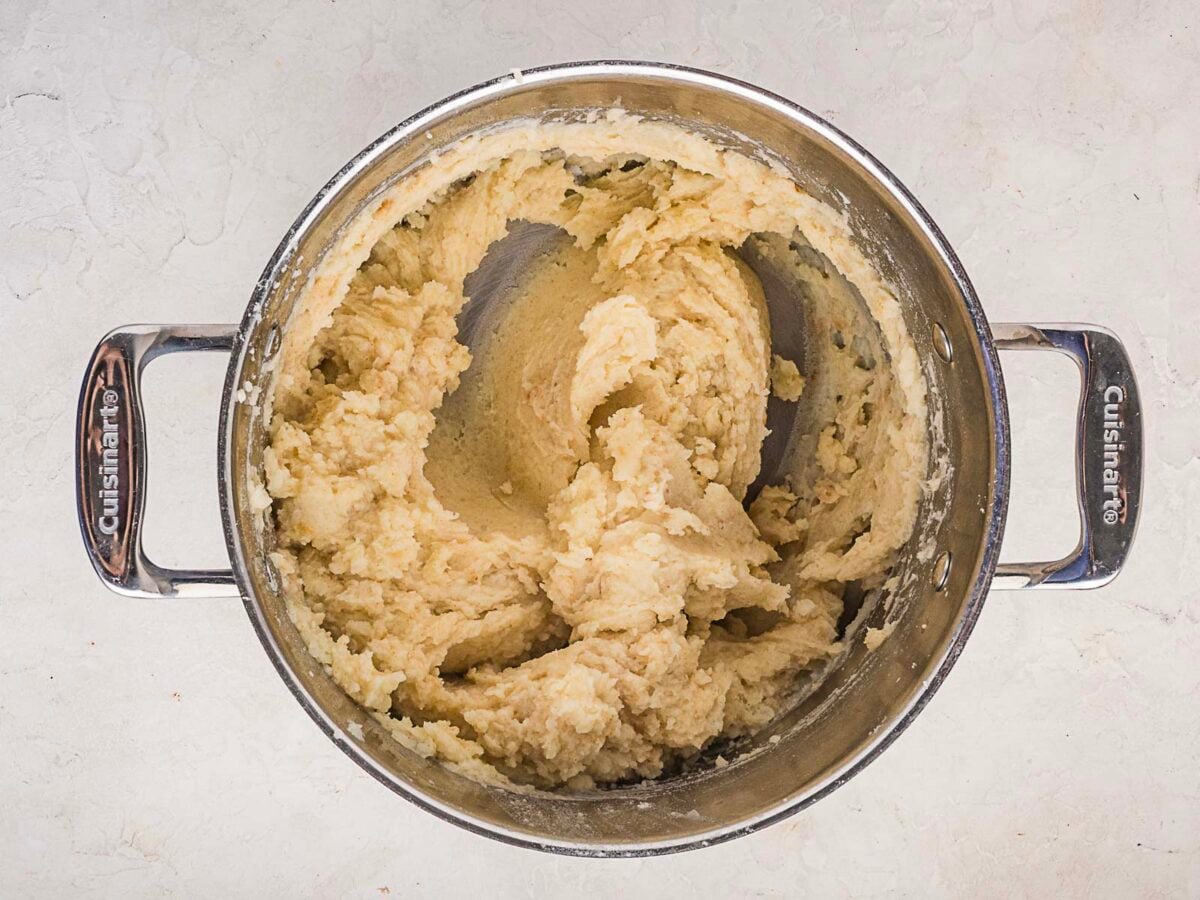 A stainless steel pot filled with creamy mashed potatoes sits on a light-colored countertop.