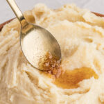 A spoon rests on mashed potatoes with melted butter pooling on top.