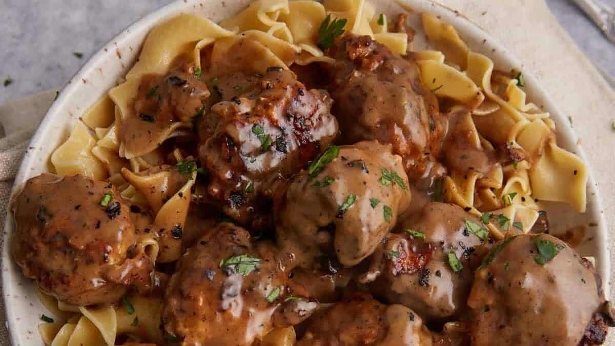 A bowl of egg noodles topped with meatballs and brown gravy, garnished with chopped parsley—a perfect choice for easy meal prep and weeknight meals.
