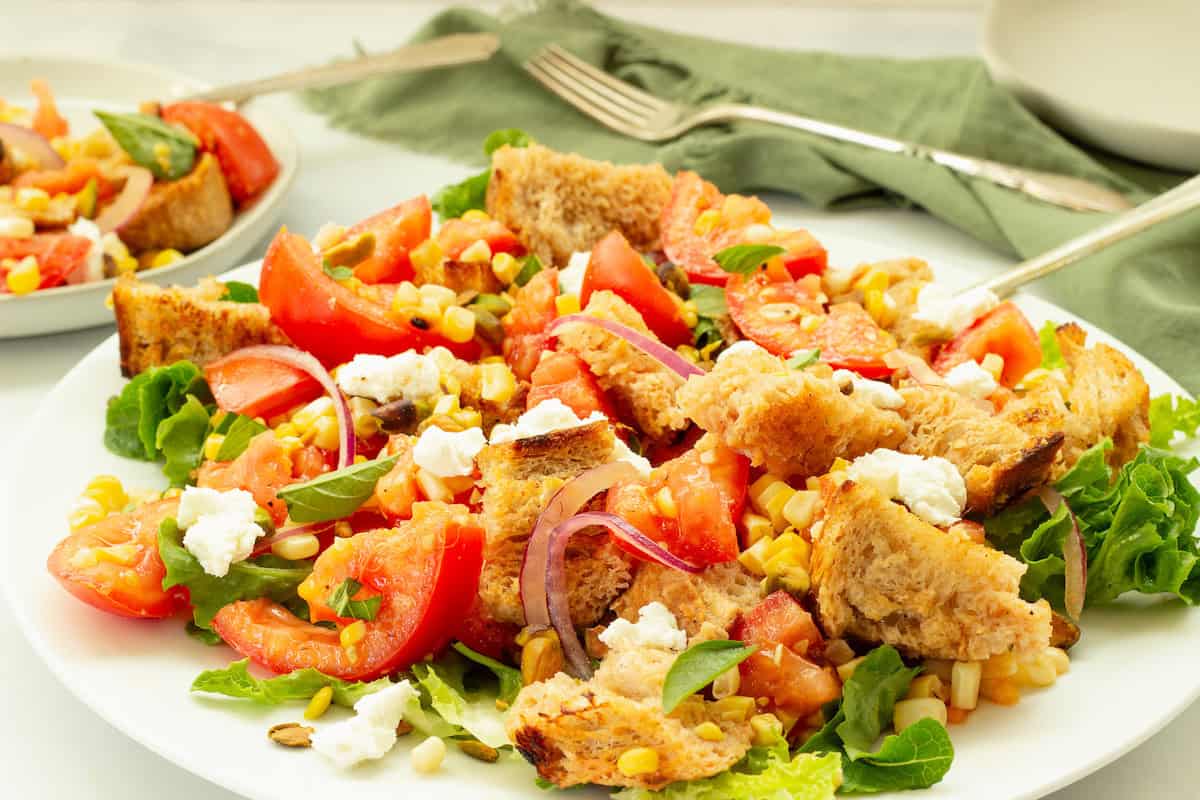 A plate of salad with lettuce, tomato, red onion, grilled bread pieces, corn, and crumbled cheese—perfect inspiration for creative Salad Recipes and hearty Fall Salads.
