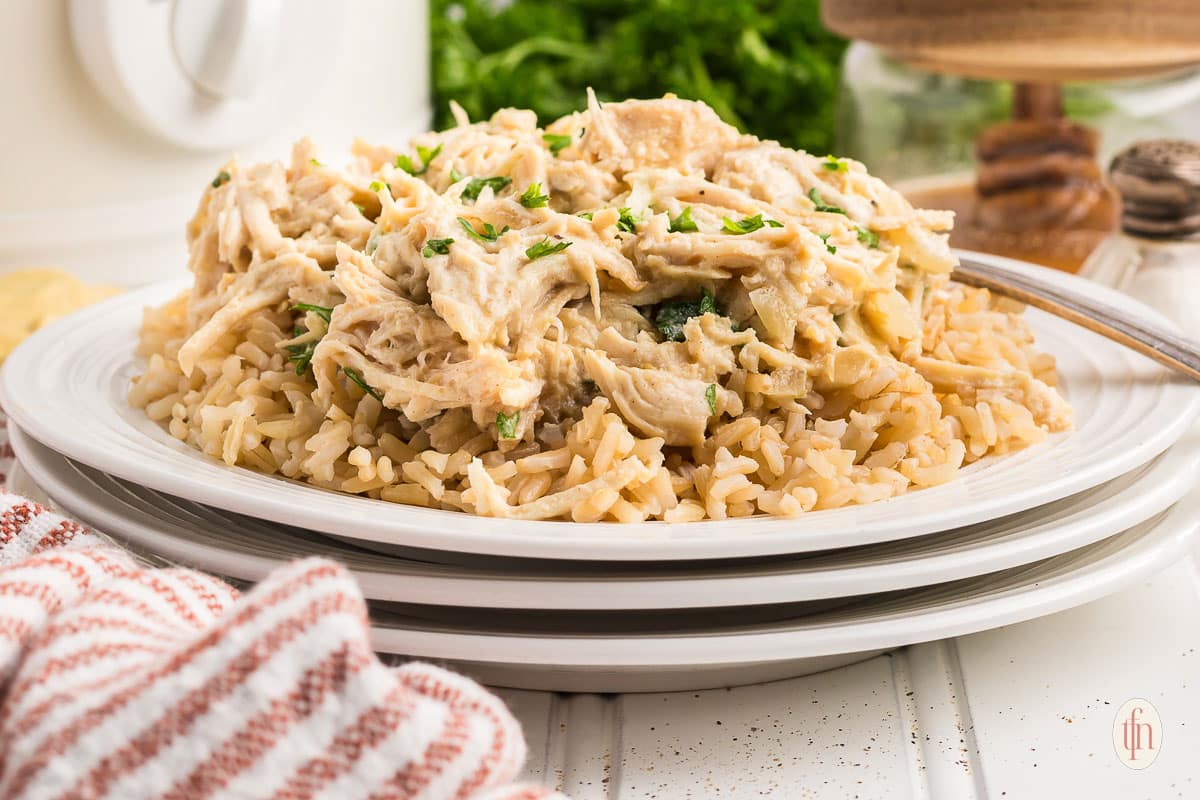 A plate of shredded chicken in a creamy sauce served over a bed of cooked rice, garnished with chopped herbs, with a fork on the side—perfect for those who love hearty savory recipes.