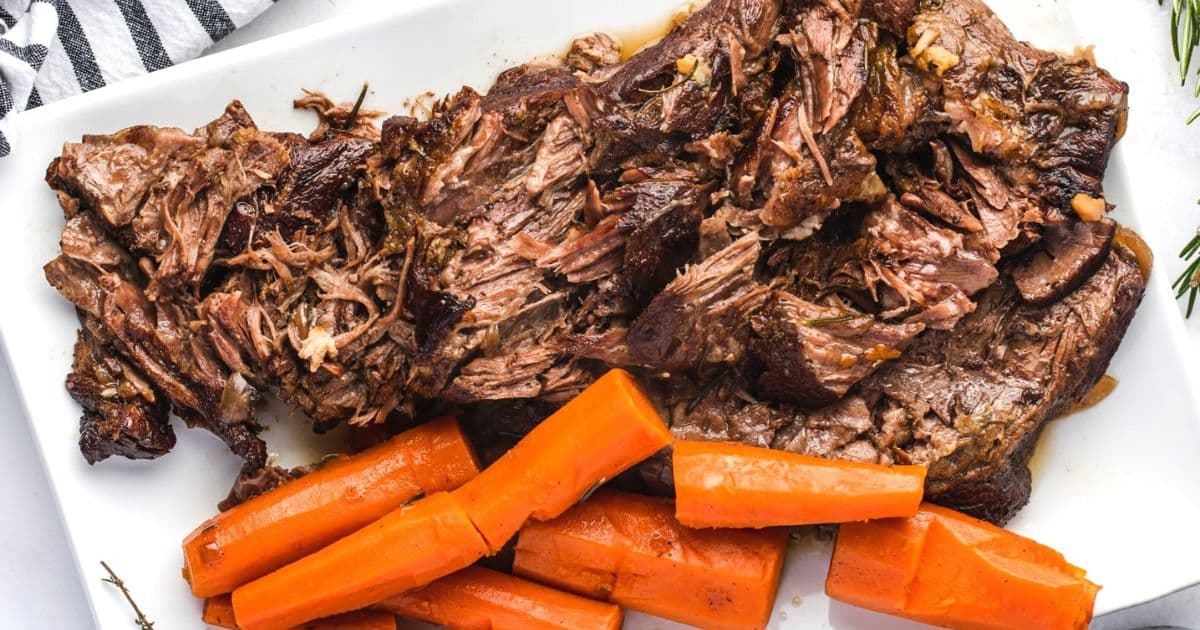 Shredded pot roast and large cooked carrot pieces arranged on a white rectangular plate—a perfect example of cooking basics for those learning essential recipes.