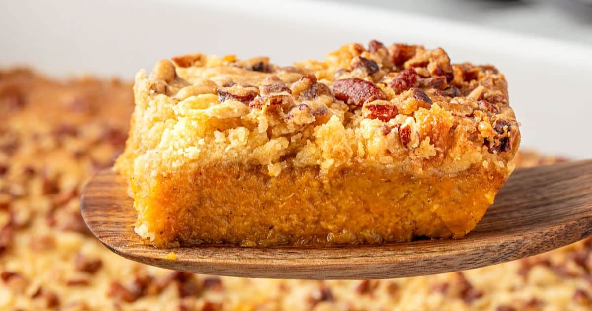 A close-up of a slice of pumpkin crunch cake with a crumbly pecan topping on a wooden spatula—a perfect non-casserole treat for fans of sweet potato recipes.