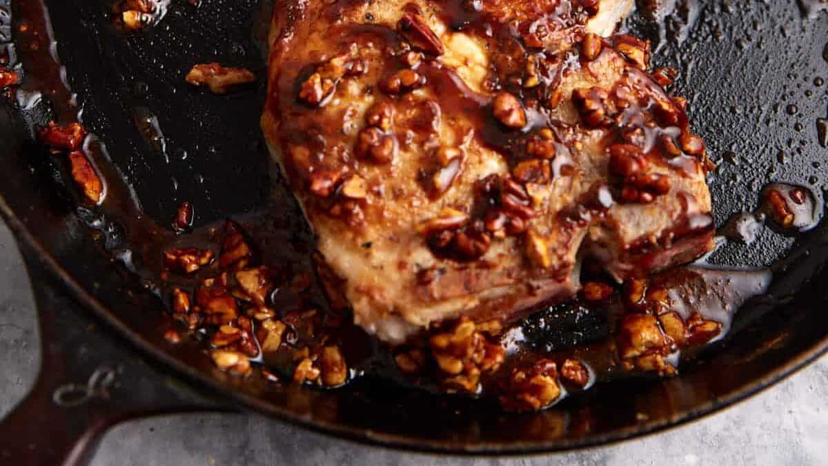 Pork chop in a skillet topped with a brown glaze and chopped pecans, with sauce pooling around the meat—a perfect example of sweet and savory recipes that elevate classic dishes.