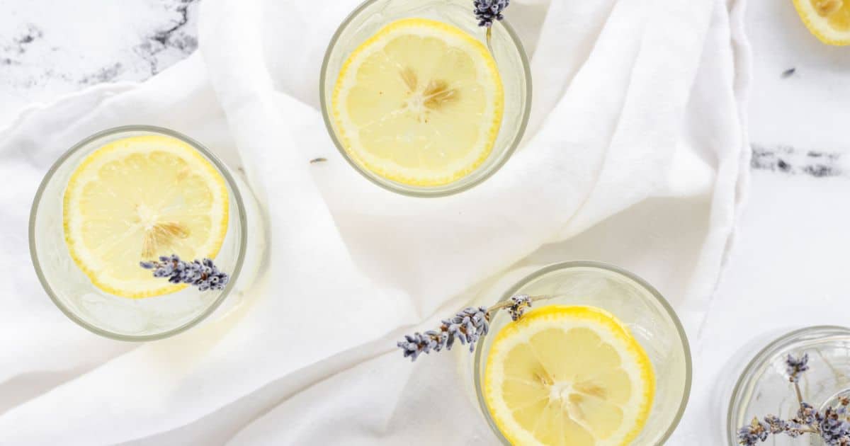 Three glasses of lemonade with lemon slices and sprigs of lavender on a white cloth, viewed from above—a refreshing idea for brunch drinks or light brunch cocktails.