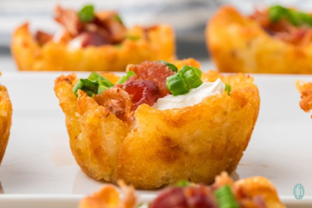 A crispy potato cup filled with sour cream, chopped bacon, and green onions—perfect as crowd-pleasing appetizers served on a white plate.