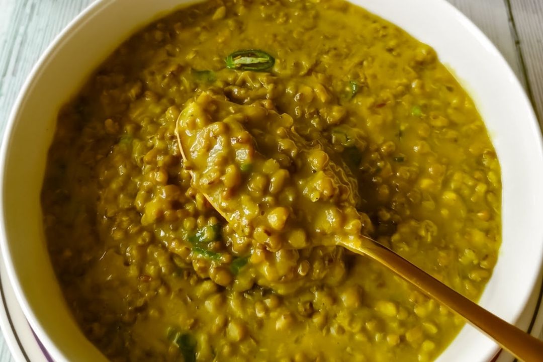 A bowl of cooked green moong dal with a thick, yellowish-green consistency, garnished with chopped green chilies, with a spoon scooping some dal—an inviting example of comforting bean soups that warm both heart and soul.